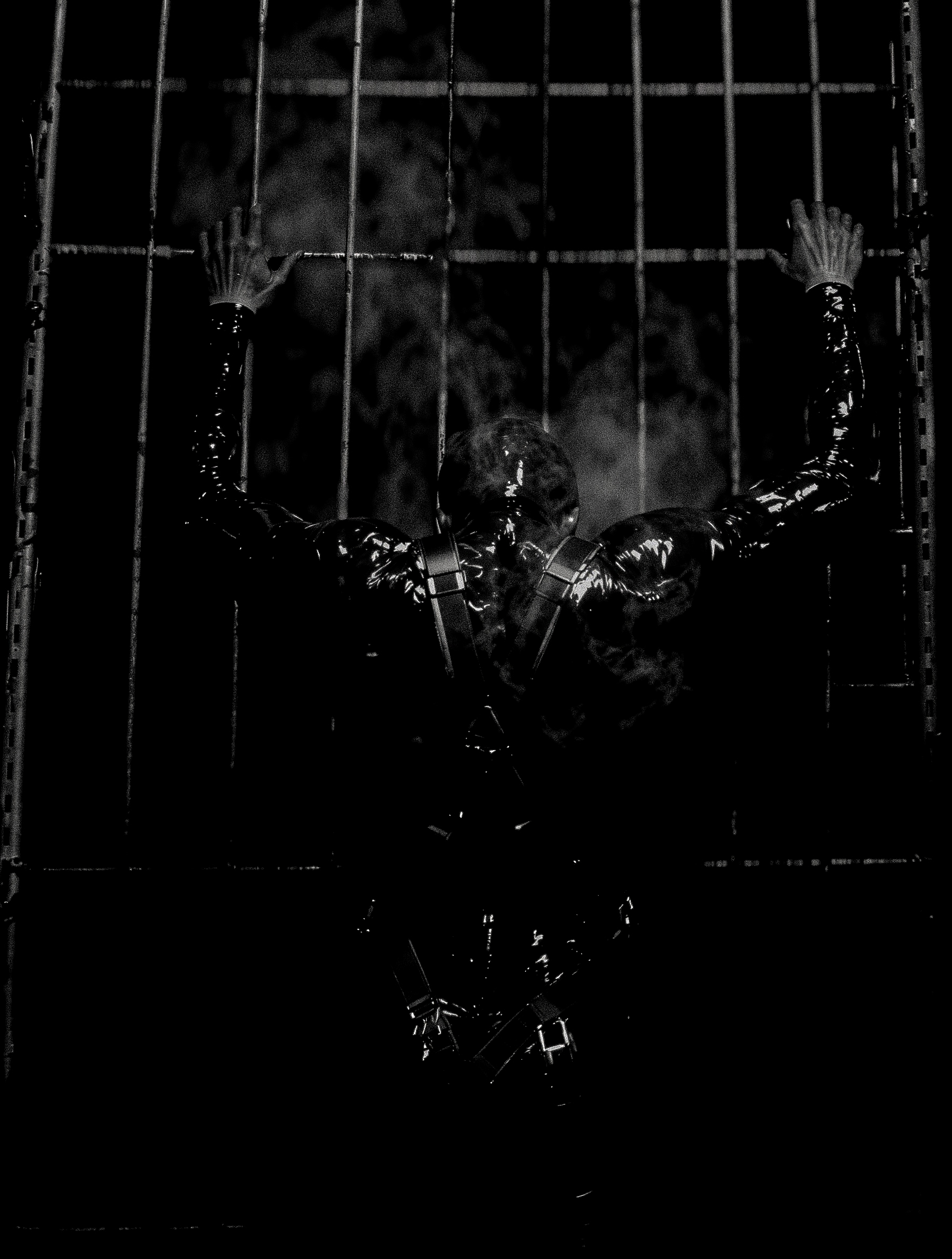 Person in latex and harness gripping the bars of a cage, lit hard in black and white