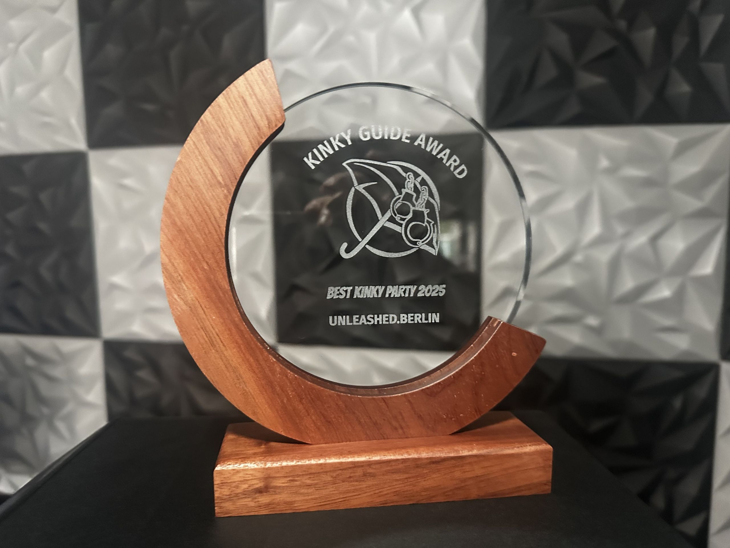 Die gravierte Glas-Trophäe des Kinky Guide Award — „Best Kinky Party 2025, UNLEASHED.BERLIN“ mit dem Regenschirm-und-Handschellen-Logo